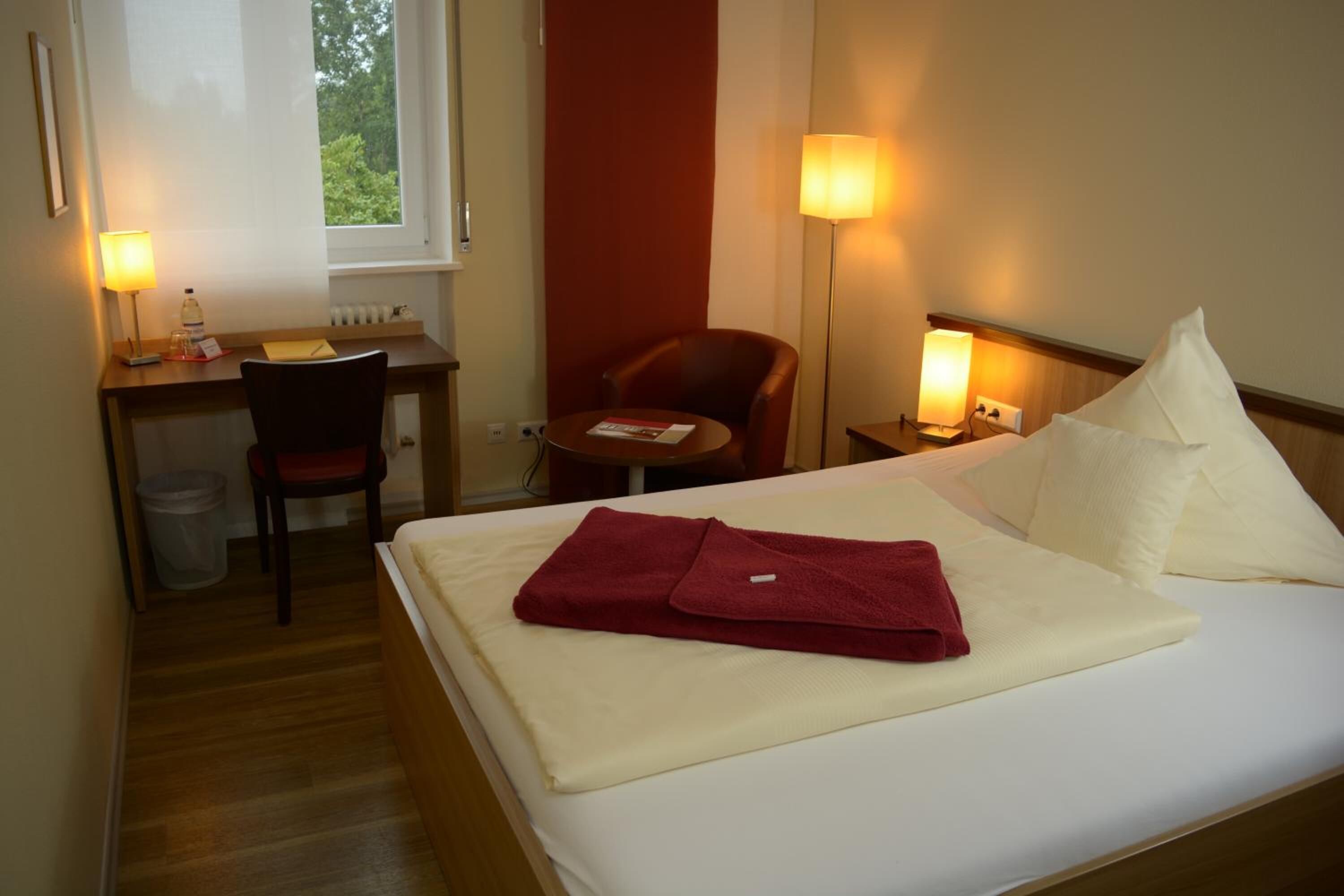 Una habitación de hotel con una cama, un escritorio, una silla y una mesita de noche con lámpara.