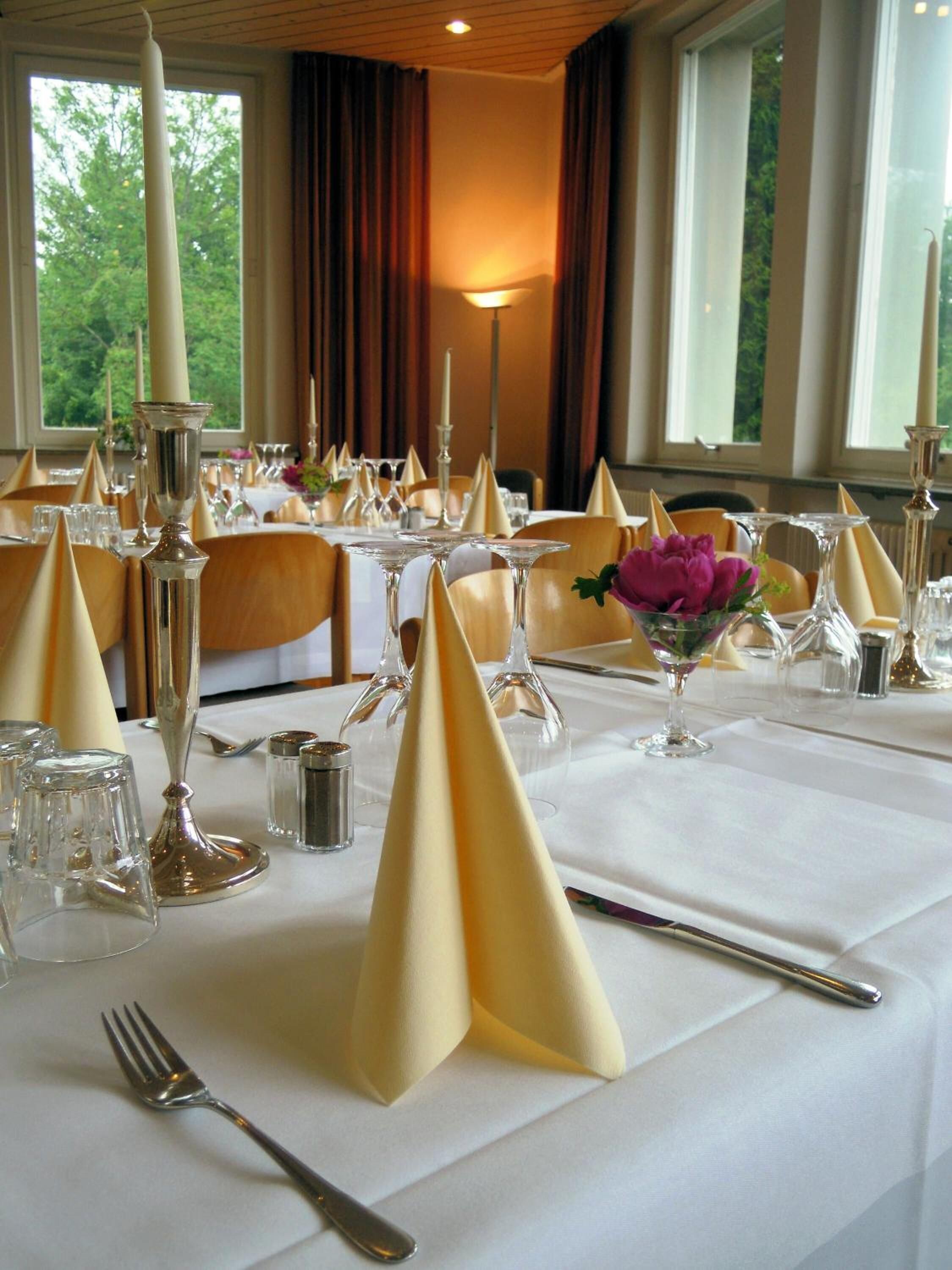 A table set for a formal dinner with white tablecloths, gold napkins, and candle holders.