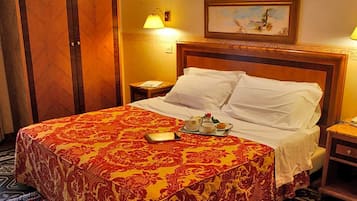 Una camera d'hotel con un letto grande, due comodini, un tavolino e un quadro appeso al muro, con una lampada su ciascun tavolino.