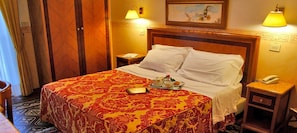 A hotel room with a large bed, two bedside tables, a nightstand, a painting on the wall, and a lamp on each table.