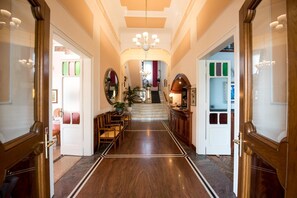A grand hallway with a marble floor, wooden doors, and a staircase leading to an upper level.
