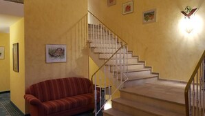 A staircase with a white railing, a red striped sofa, and framed pictures on the walls. - Hotel und Restaurant Moosmühle (Dietenhofen)