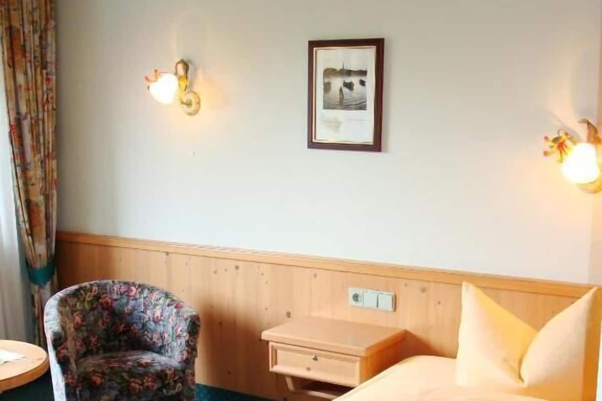 Quarto de hotel com cama, cadeira, mesa de cabeceira e luminária na parede.