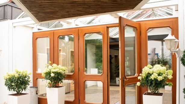 A wooden double door with glass panels, flanked by white planters with green plants. - Hotel und Restaurant Moosmühle (Dietenhofen)