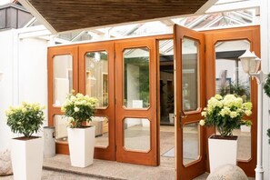 A wooden double door with glass panels, flanked by white planters with green plants. - Hotel und Restaurant Moosmühle (Dietenhofen)