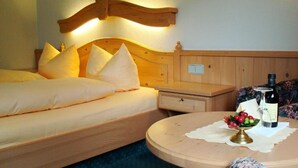 A hotel room with a wooden bed, a bedside table with a bottle and glasses, and a small table with a vase of flowers. - Hotel und Restaurant Moosmühle (Dietenhofen)