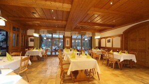 A restaurant with wooden interiors, multiple tables with white tablecloths, and yellow napkins. - Hotel und Restaurant Moosmühle (Dietenhofen)