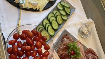 Una mesa de buffet con diversos alimentos, entre ellos queso, pepinos, tomates cherry y carnes.