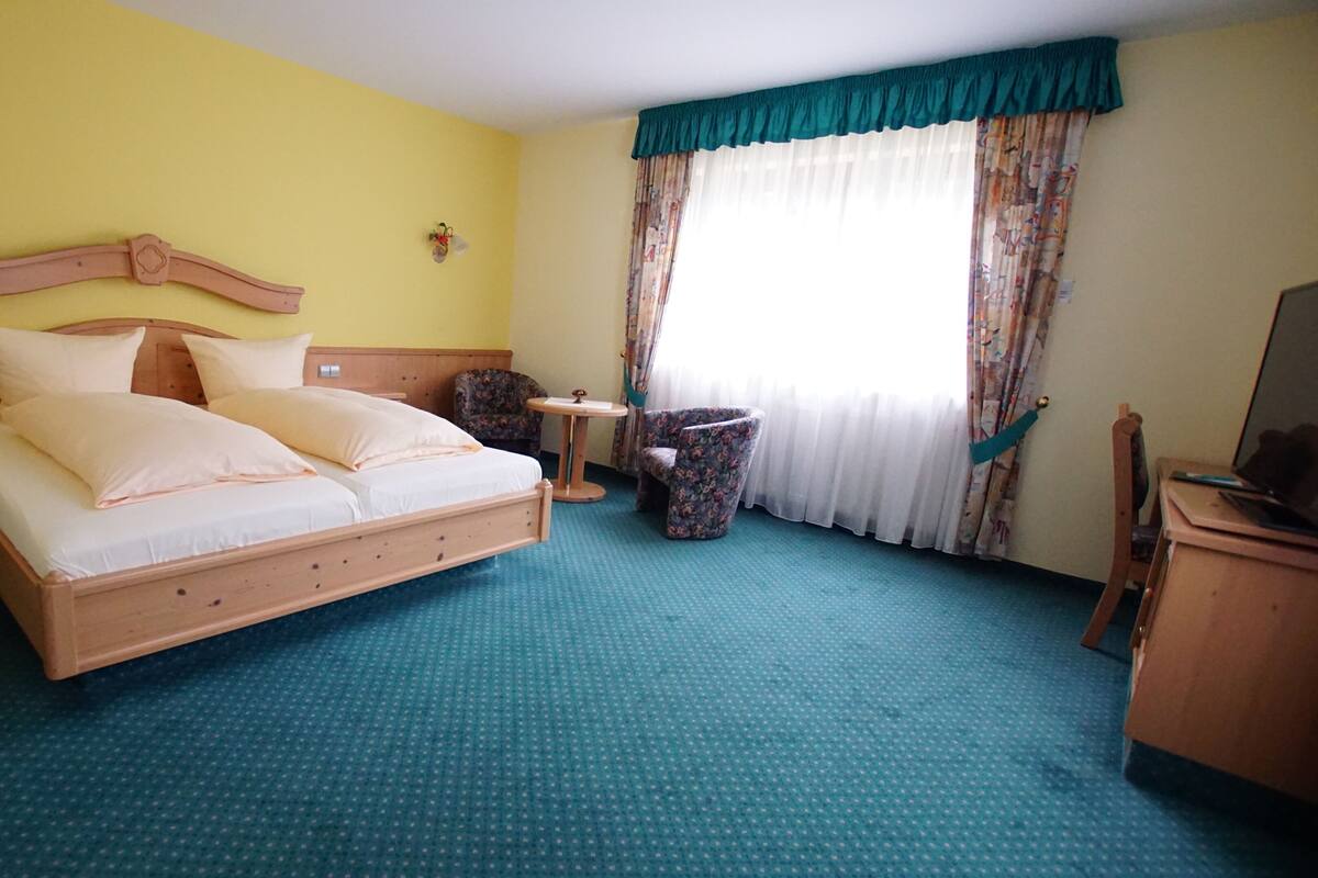 Quarto de hotel com uma cama grande, uma mesa pequena, uma cadeira e uma escrivaninha com um computador.