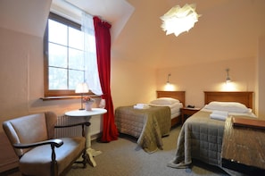 A hotel room with two beds, a chair, a table with a lamp, and a window with curtains.