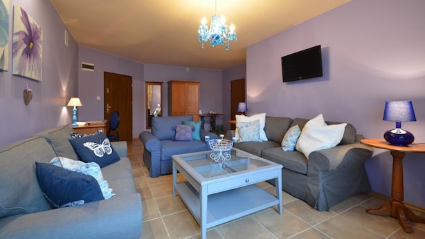 A living room with two sofas, a coffee table, a chandelier, a television, and a wall-mounted TV. - Dworek Nad Reg O (Trzebiatow)