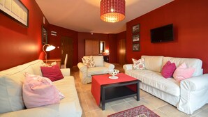 A living room with red walls, white sofas, and a chandelier. - Dworek Nad Reg O (Trzebiatow)