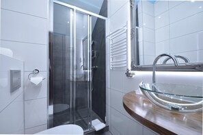 Un baño moderno con cabina de ducha de vidrio, inodoro blanco y lavamanos de vidrio sobre encimera de madera.
