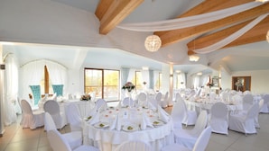 A banquet hall with round tables, white chairs, and a high ceiling with exposed wooden beams. - Dworek Nad Reg O (Trzebiatow)