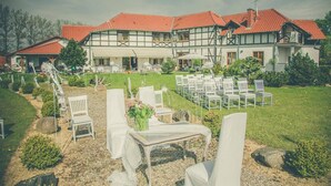 A traditional building with a red-tiled roof and a garden with white chairs and tables. - Dworek Nad Reg O (Trzebiatow)