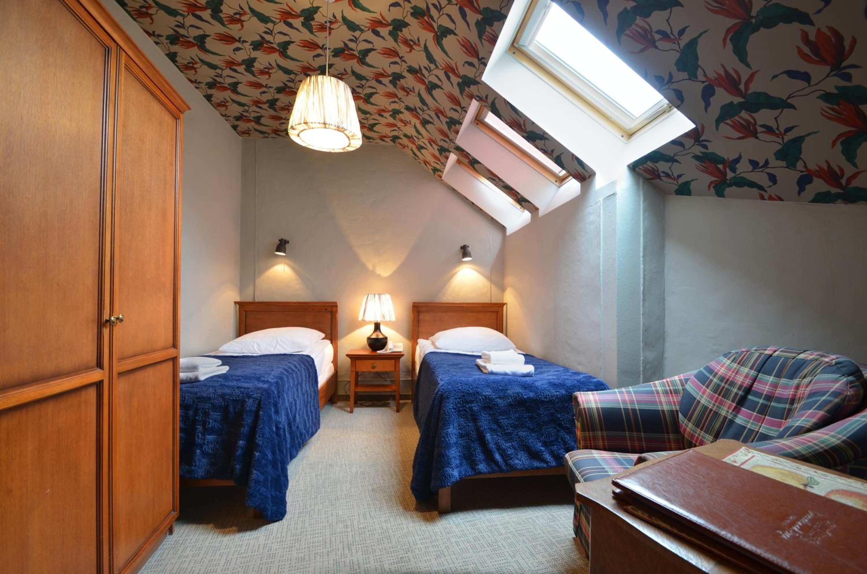 Un dormitorio con dos camas, una mesita de noche con lámpara, un armario de madera y un tragaluz.