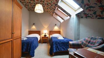 Un dormitorio con dos camas, una mesita de noche con lámpara, un armario de madera y un tragaluz.