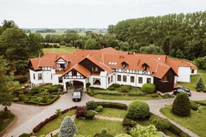 A large, multi-story building with a red-tiled roof, surrounded by well-maintained gardens and trees. - Dworek Nad Reg O (Trzebiatow)