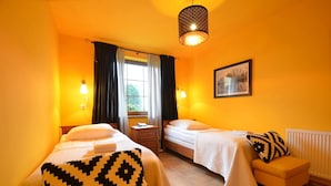 A hotel room with two beds, a window with curtains, a hanging light fixture, a bedside table, a chair, and a framed picture on the wall. - Dworek Nad Reg O (Trzebiatow)
