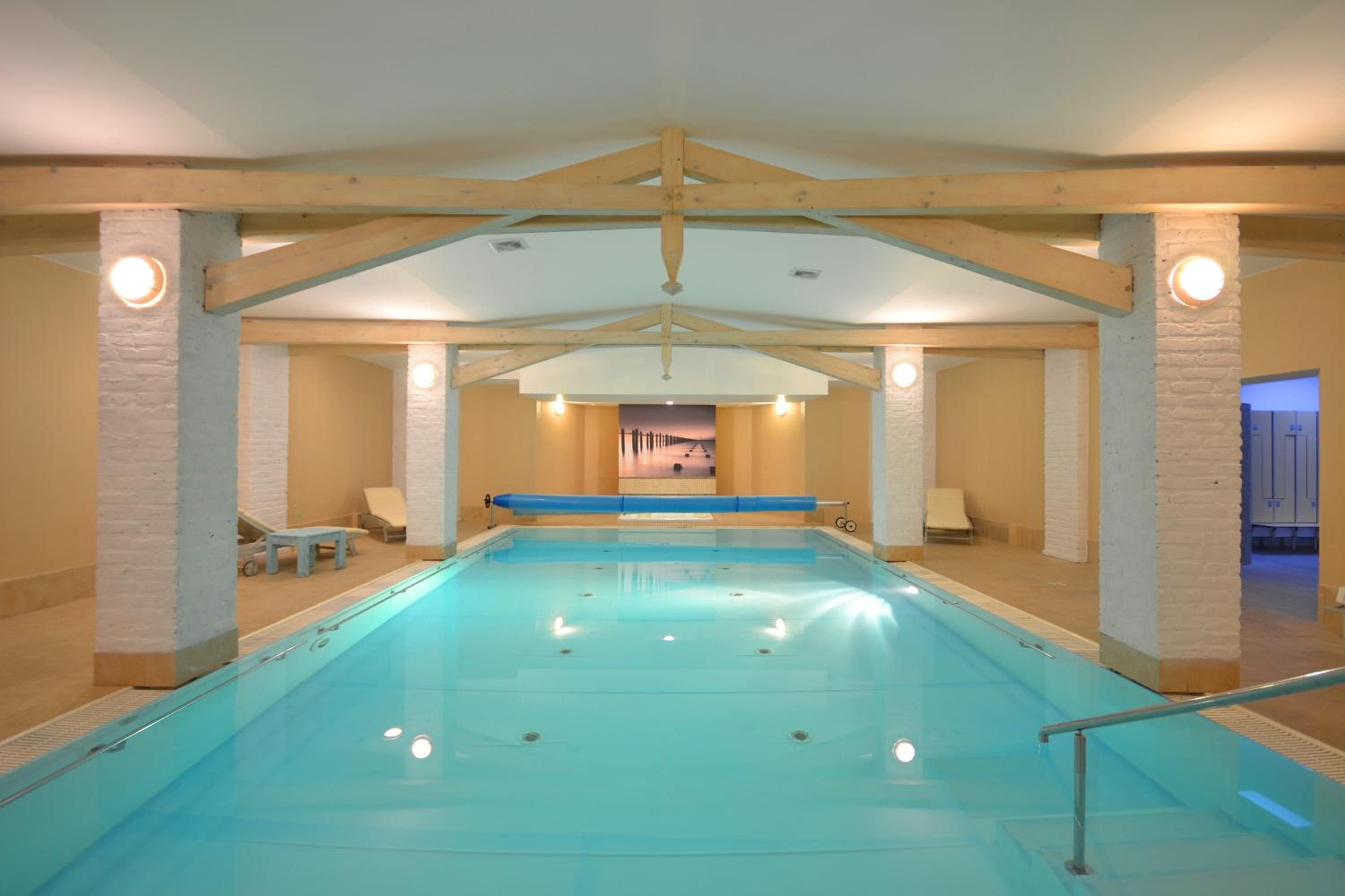 Una piscina interior con vista despejada al área de la piscina, sillas de descanso y una puerta que conduce a otra habitación.