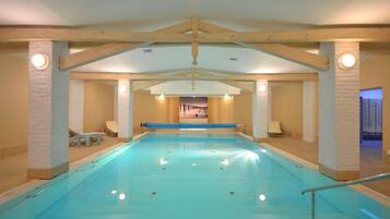 Una piscina interior con vista despejada al área de la piscina, sillas de descanso y una puerta que conduce a otra habitación.