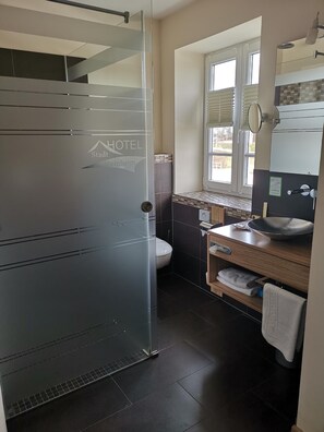 Un baño moderno con cabina de ducha de vidrio, inodoro, lavamanos con espejo y ventana que proporciona luz natural.