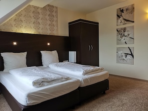 A double bed with white linens in a room with dark wood headboard, a dark wardrobe, and wall-mounted artwork.