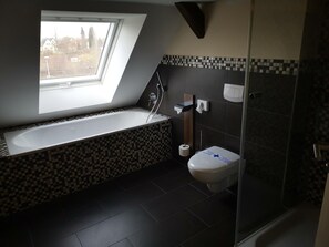 A modern bathroom with a skylight, a bathtub, a toilet, and a shower area.