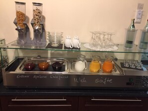 Un buffet proposant une variété de plats et de boissons, notamment des pots de confitures et des carafes de boissons.
