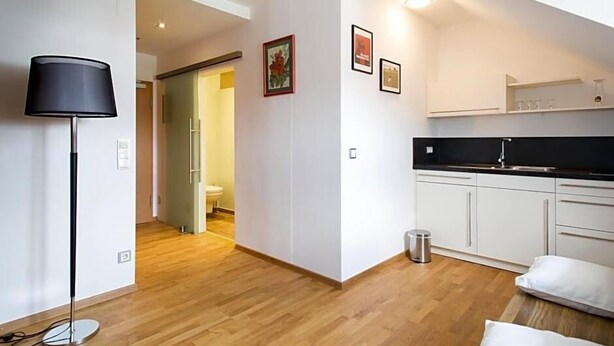 A modern kitchen with white cabinets, a black countertop, and a small trash can. - Landhotel Grv Nenbach (Bad Groenenbach)
