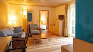 A modern hotel room with a sofa, armchair, small table, and a TV. - Landhotel Grv Nenbach (Bad Groenenbach)