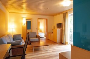 A modern hotel room with a sofa, armchair, small table, and a TV.