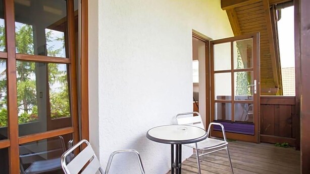 Un espacio de estar al aire libre cubierto, con una mesa, sillas, ventanas amplias y una terraza de madera.