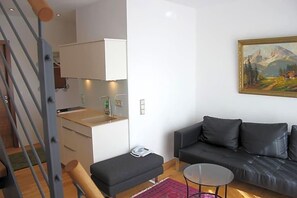 A modern living room with a sofa, a small round table, a bench, and a painting on the wall.