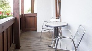 Un balcón de madera con una mesa y sillas, una barandilla de madera y una ventana con persianas.