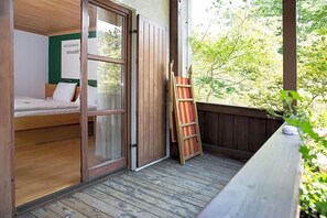 A room with a bed, a wooden ladder, and a view of greenery outside.