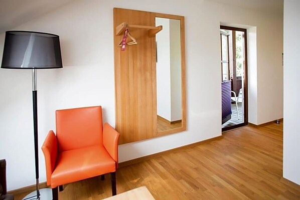A room with a wooden floor, a single orange chair, a floor lamp, and a large mirror on the wall.