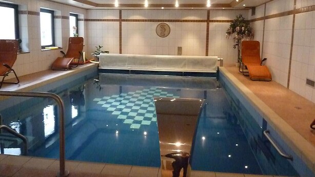Une piscine intérieure avec des carreaux de sol à motifs, des chaises longues et un banc.
