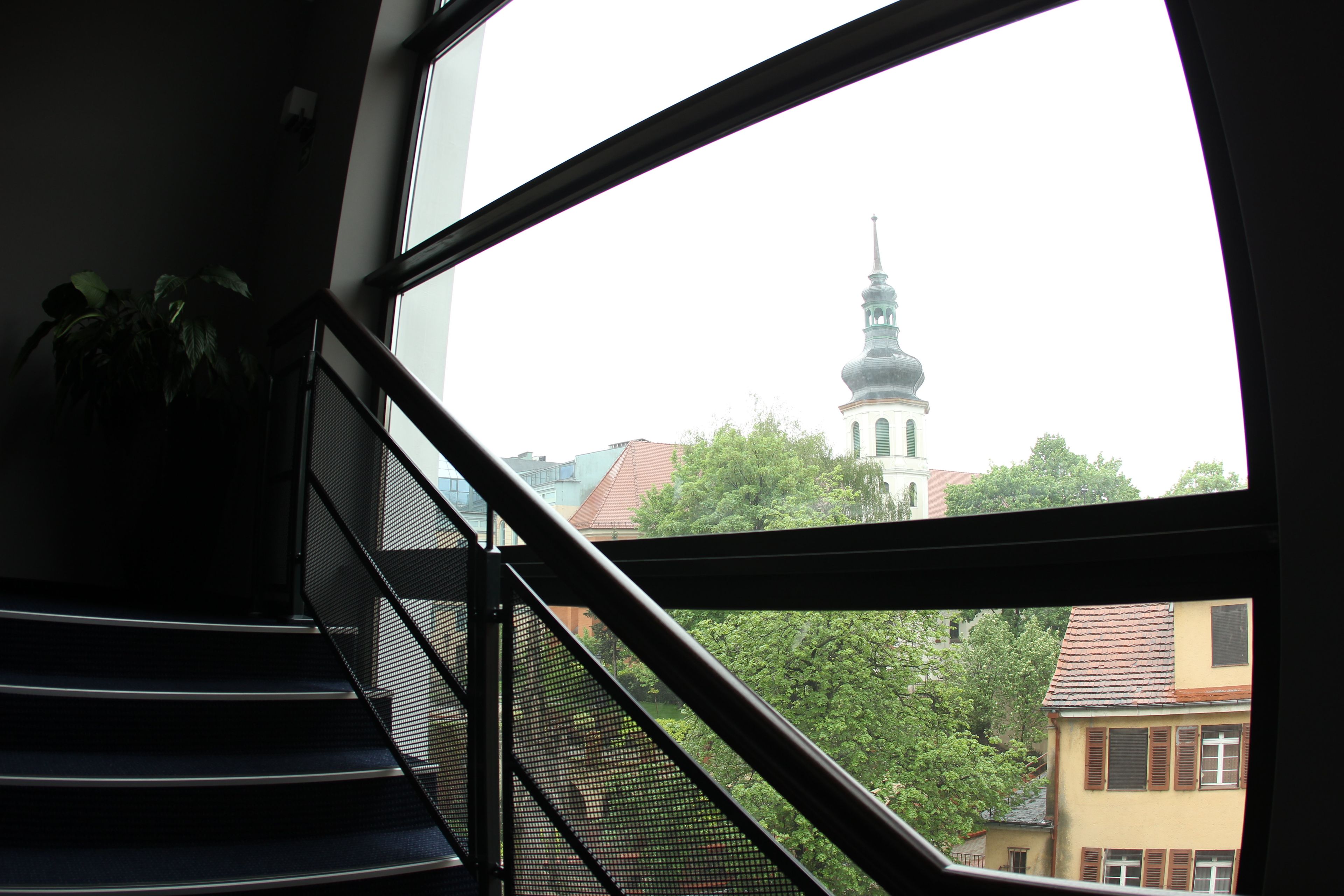 Eine Treppe mit Metallgeländer führt zu einem Fenster mit Blick auf ein Gebäude mit einem Turm.