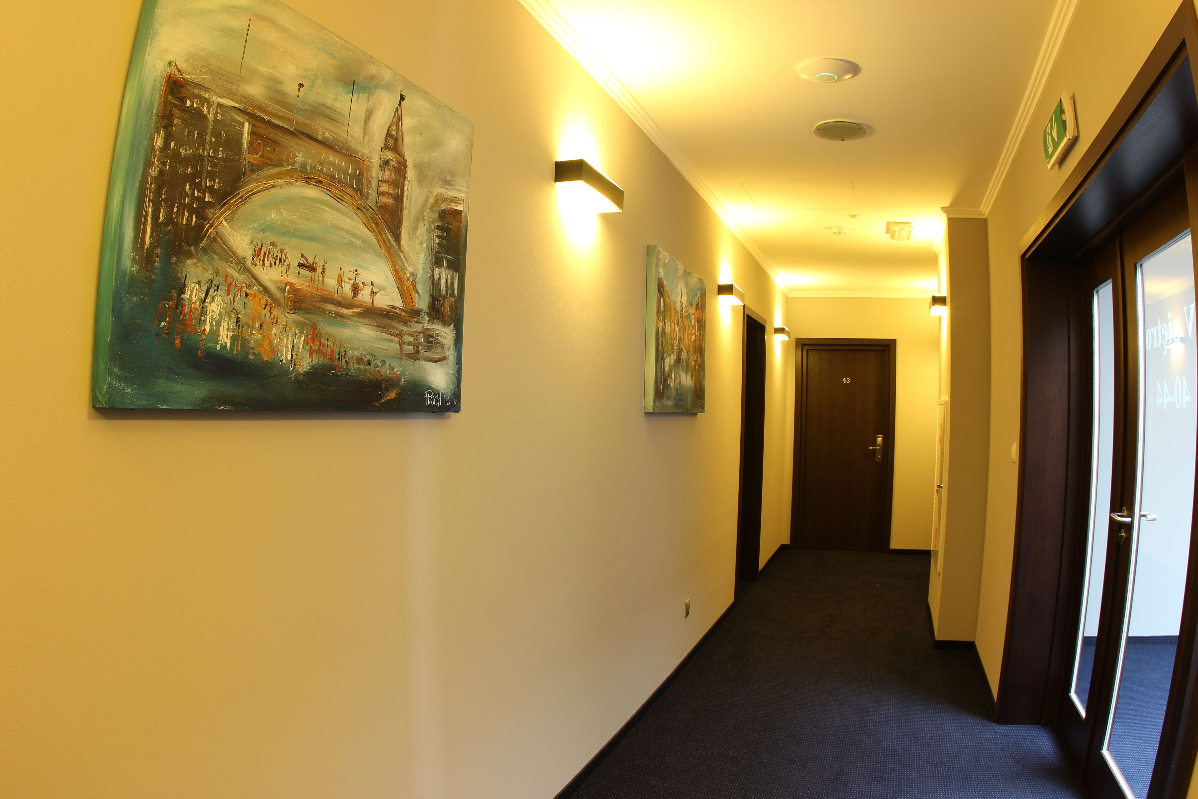 Ein Hotelkorridor mit Kunstwerken an den Wänden, einem Teppichboden und einer Tür am Ende.