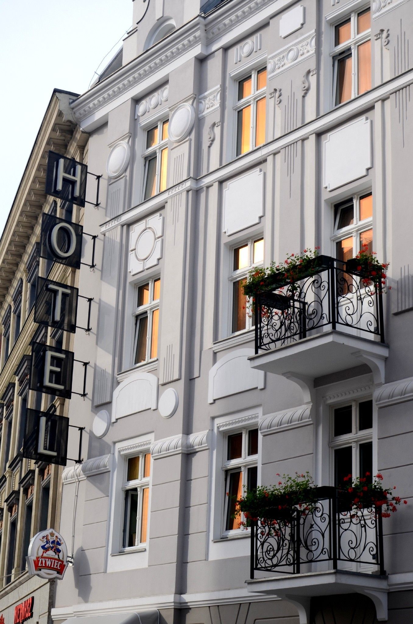 Eine Hotels Fassade mit einer auffälligen Schrifttafel, dekorativen Balkonen mit Blumenkästen und klassischer Architektur.