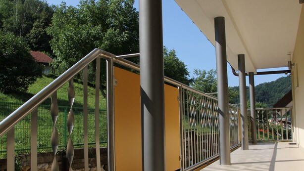 A covered outdoor staircase with metal railings, beige steps, and a view of greenery and hills in the background. - Apartments Veno (Lasko)