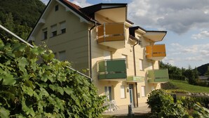 A two-story building with a balcony on the second floor, a door with a sign, and a view of a green landscape. - Apartments Veno (Lasko)