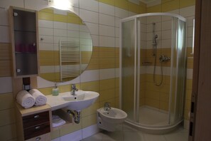 A bathroom with a curved shower enclosure, a sink, and a bidet.