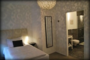 A hotel room with a bed, bedside table, lamp, and a large mirror.