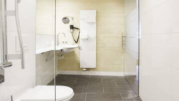 Een moderne badkamer met een glazen douchecabine, een wit toilet en een donkere betegelde vloer.