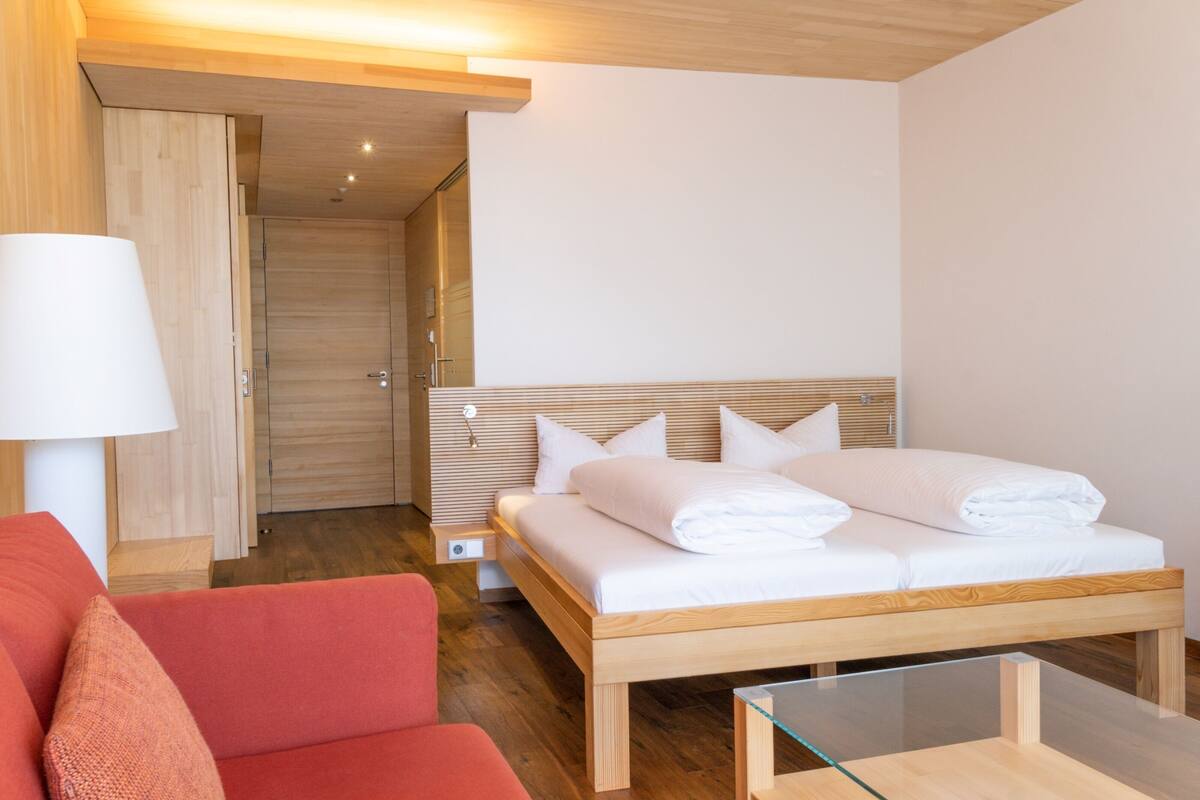 A modern hotel room with a wooden bed, a red sofa, and a glass coffee table.