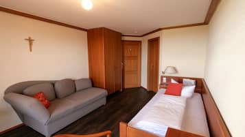 Una habitación con una cama, un sofá, una silla de madera, una cruz en la pared y una puerta.