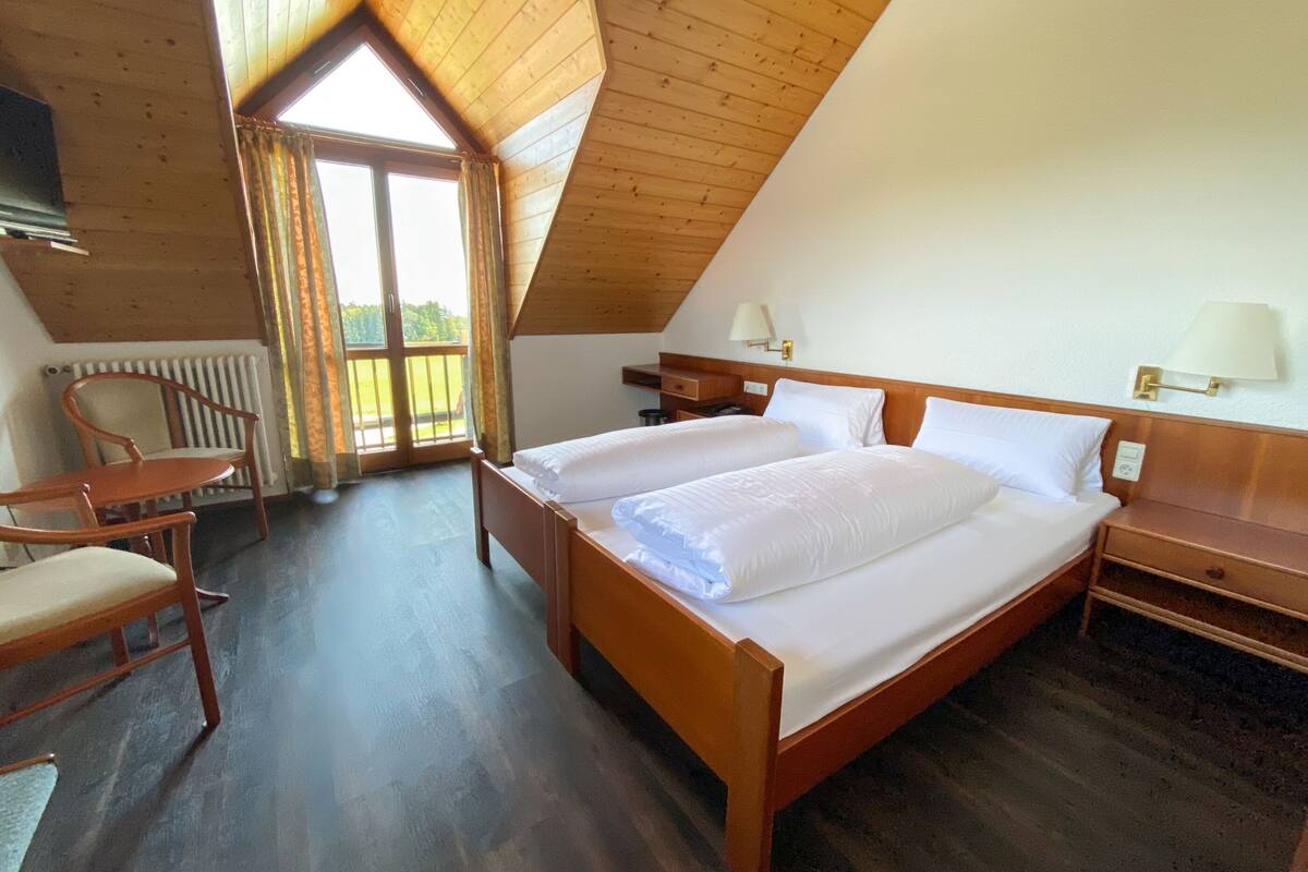 A bedroom with a large bed, a chair, a nightstand, and a window with curtains.
