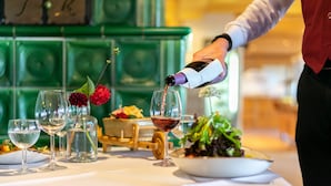 Una mesa servida con copas de vino, una botella siendo servida y un bol de ensalada.